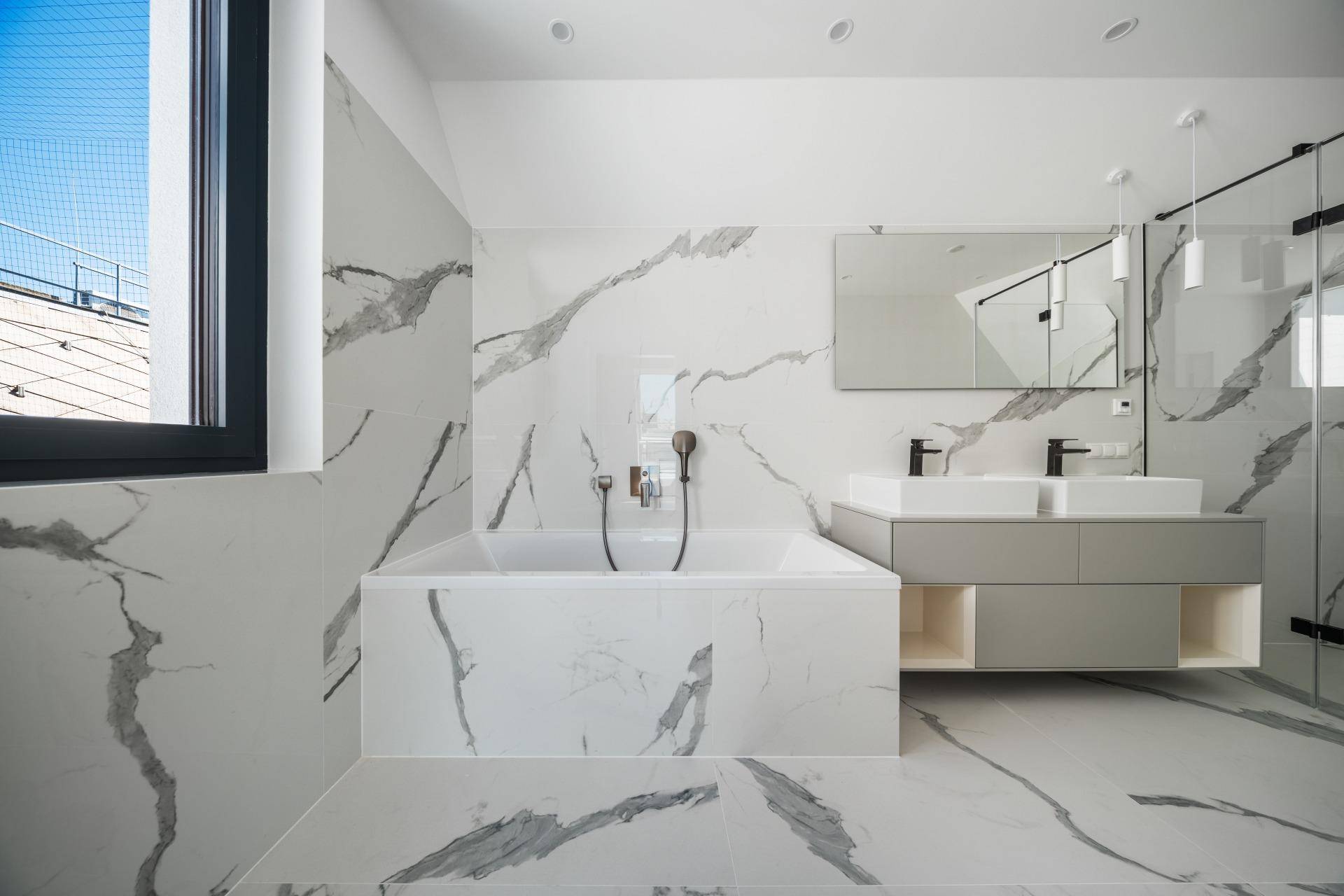 Elegantes Badezimmer mit Marmorfliesen, Badewanne und großem Fenster für viel Tageslicht.