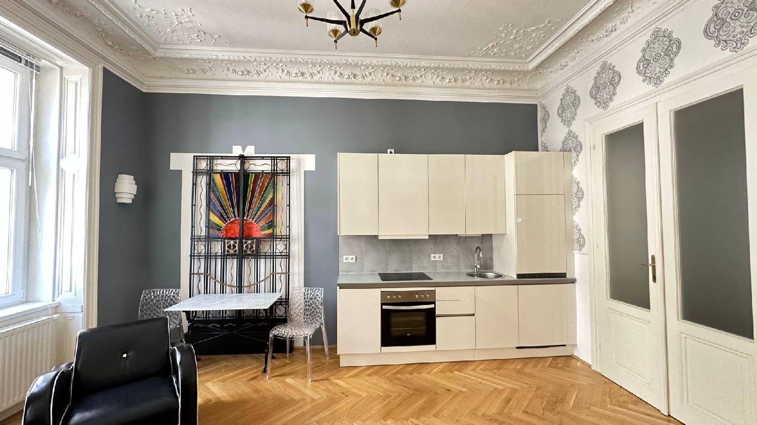 Offener Wohnbereich mit integrierter Küche, Fischgrätparkett und dekorativem Fenstergitter.