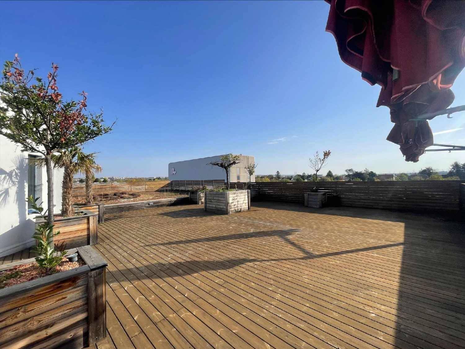Geräumige Dachterrasse mit Holzdeck, Pflanzen und Sonnenschirmen unter blauem Himmel.