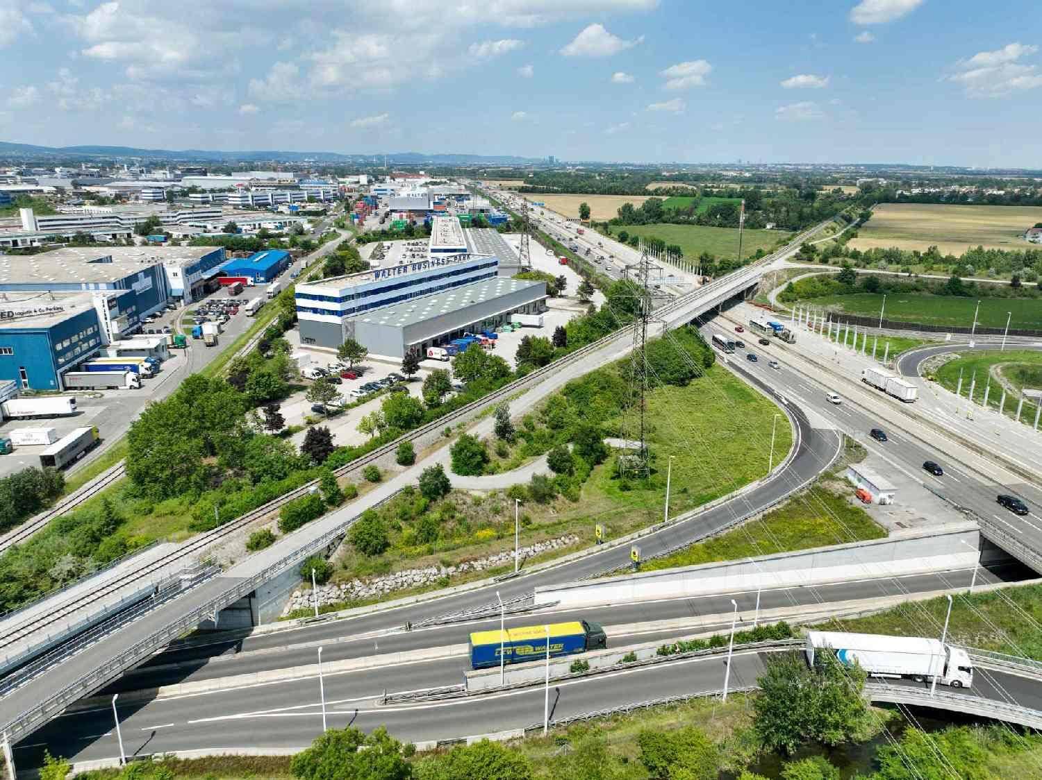 Luftaufnahme eines Geschäftsparks mit Autobahnkreuz, Industriegebäuden und weiten Grünflächen.