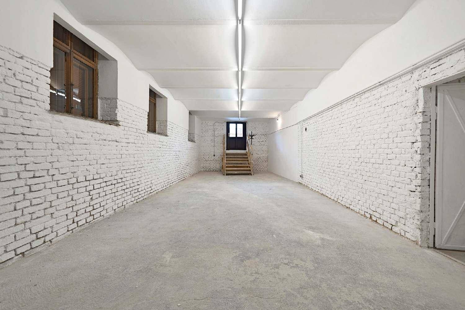Geräumiger Lagerraum mit weiß gestrichenen Ziegelwänden, Betonboden und Holztreppe zu einem Ausgang.