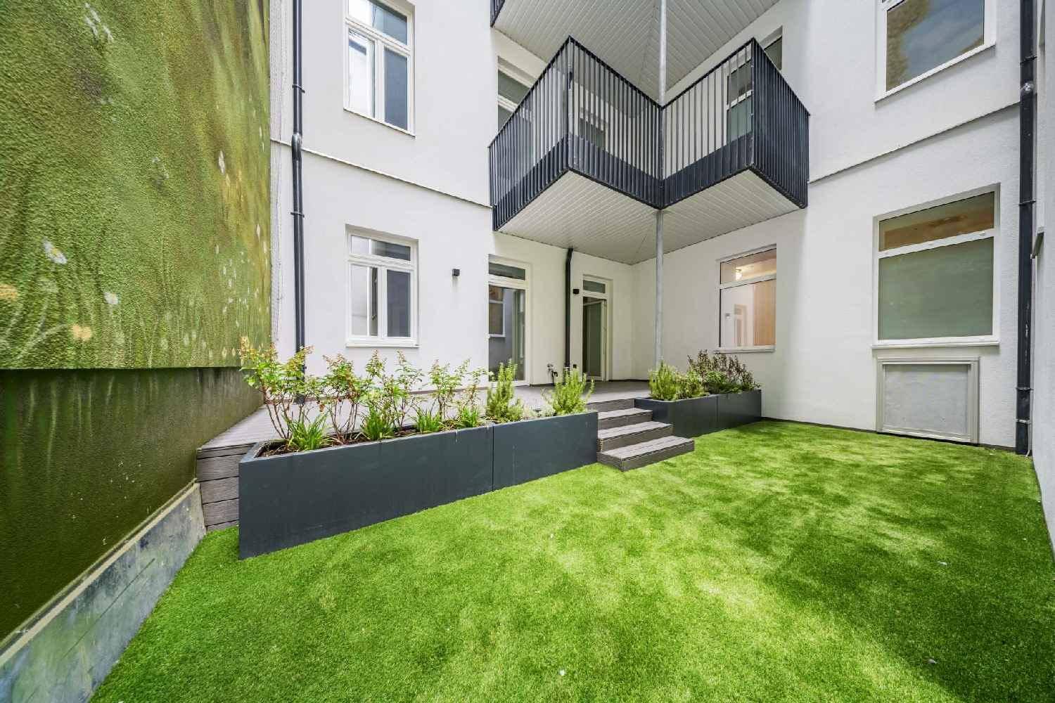 Kleiner Gartenbereich mit Kunstrasen, erhöhten Pflanzbeeten und Zugang zu einem Balkon.