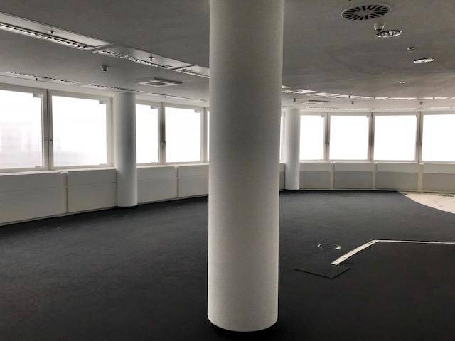 Offener Bürobereich mit dunklem Teppichboden, vielen Fenstern und einer zentralen Säule.