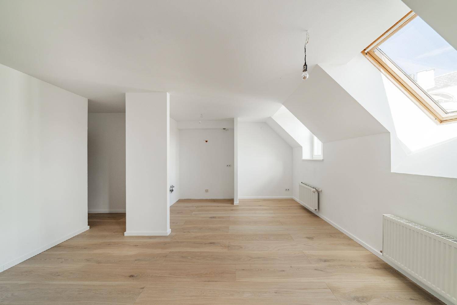 Geräumiger, unmöblierter Dachbodenraum mit Holzboden, weiß gestrichenen Wänden und einem Dachfenster.