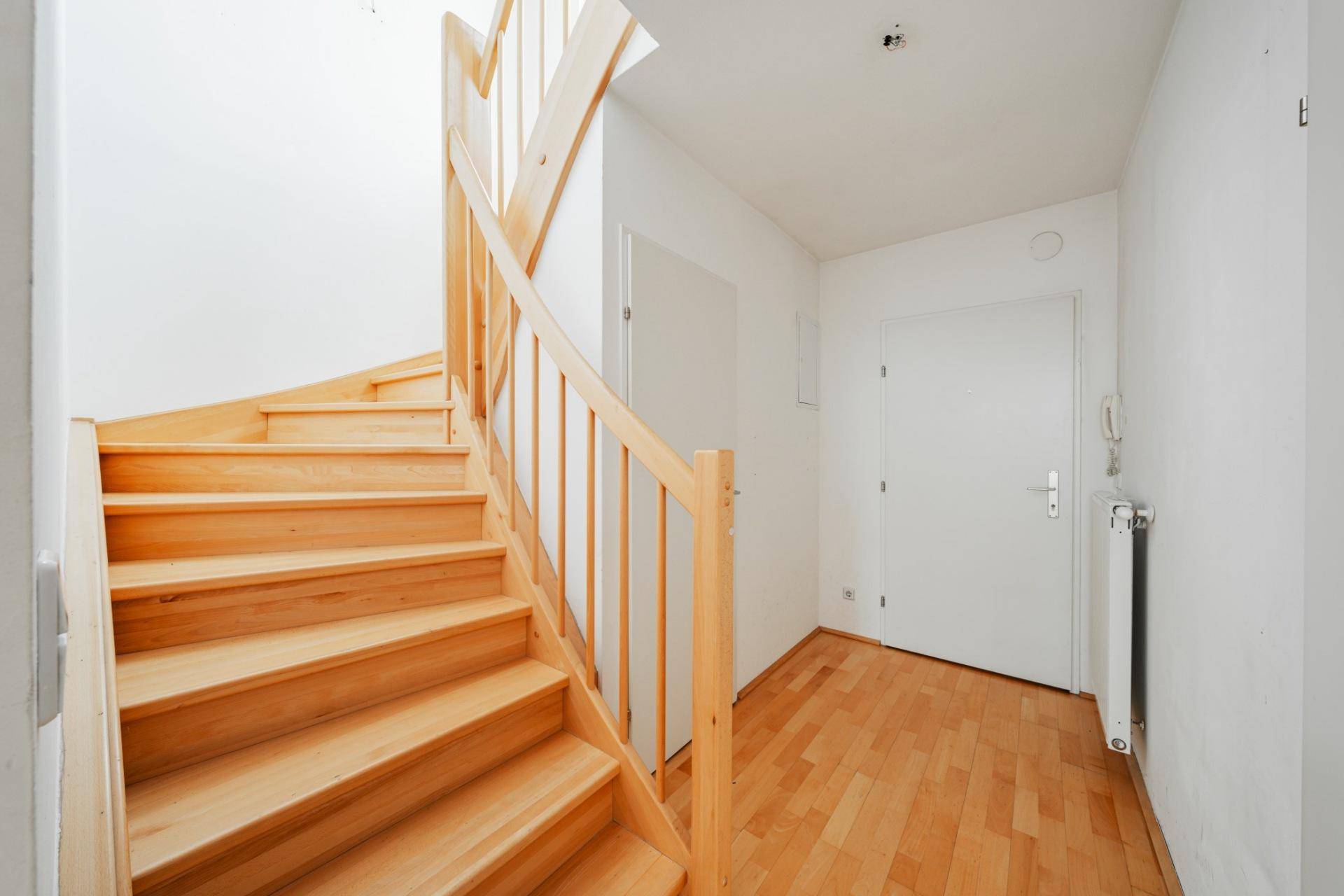 Eingangsbereich mit heller Holztreppe und Parkettboden, der zu den oberen Etagen führt.