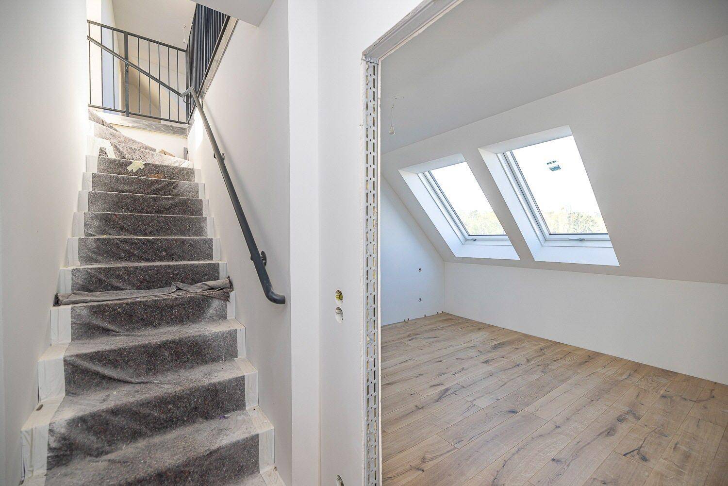 Treppenaufgang mit Schutzabdeckung und Blick in einen hellen Dachgeschossraum mit Dachfenstern.