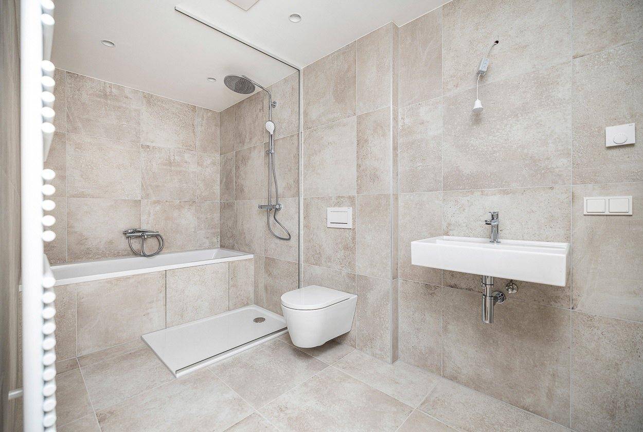 Geräumiges, modernes Badezimmer mit Badewanne, Dusche, WC und Waschbecken in hellen Grautönen.