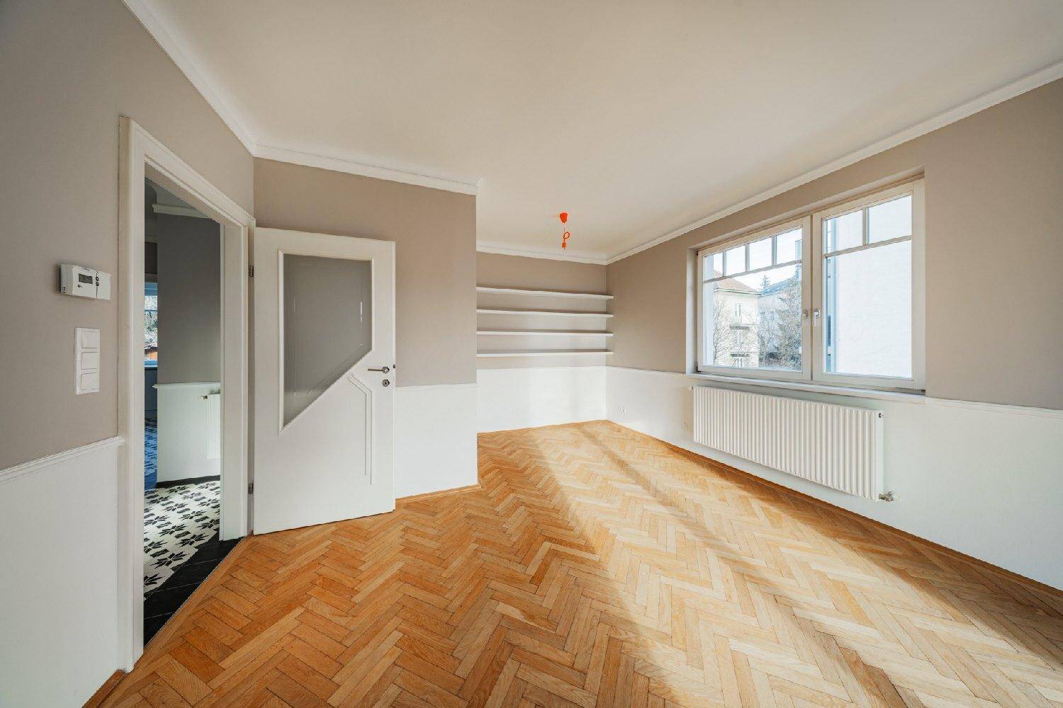 Helles Wohnzimmer mit Fischgrätparkett, praktischen Einbauregalen und einem Fenster mit Ausblick.