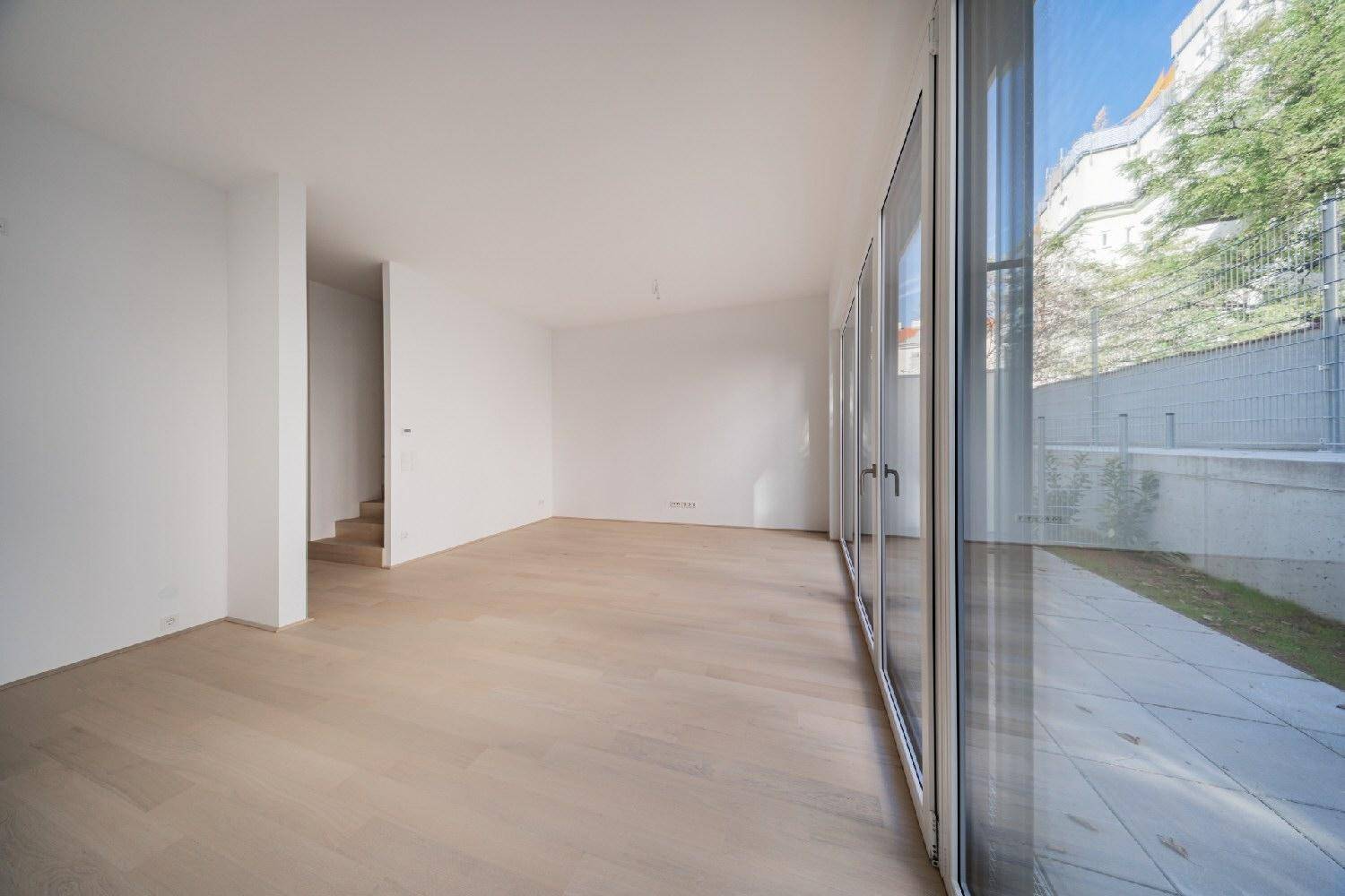 Lichtdurchfluteter Wohnraum mit Holzboden und bodentiefen Fenstern, die den Blick nach draußen freigeben.