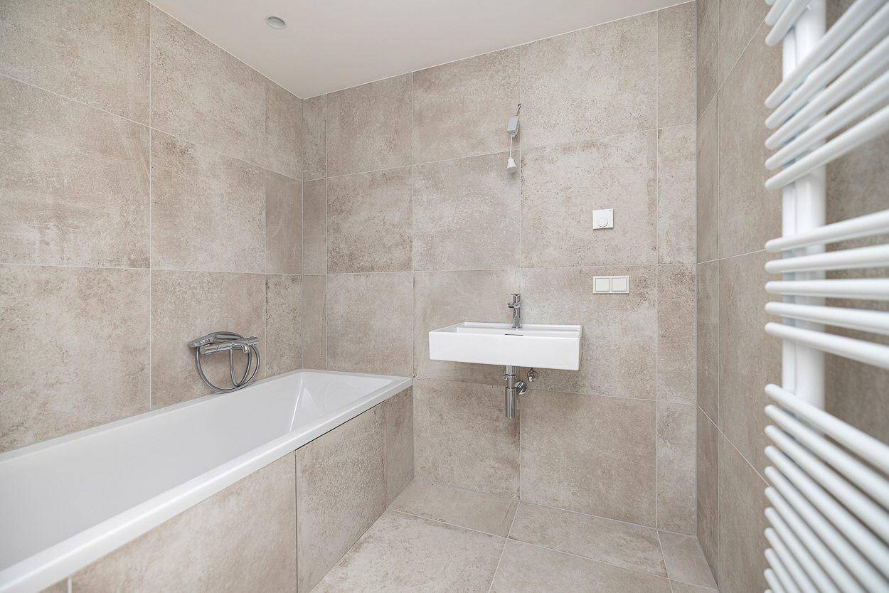 Helles Badezimmer mit beigefarbenen Fliesen, Badewanne, Einzelwaschbecken und Handtuchheizkörper.