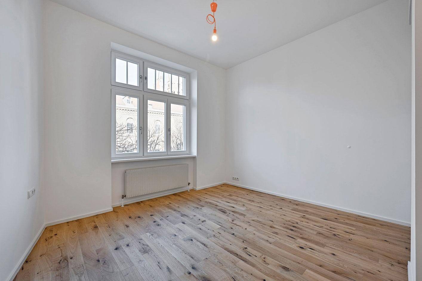Helles Schlafzimmer mit Holzboden und großem Fenster mit Blick ins Grüne.