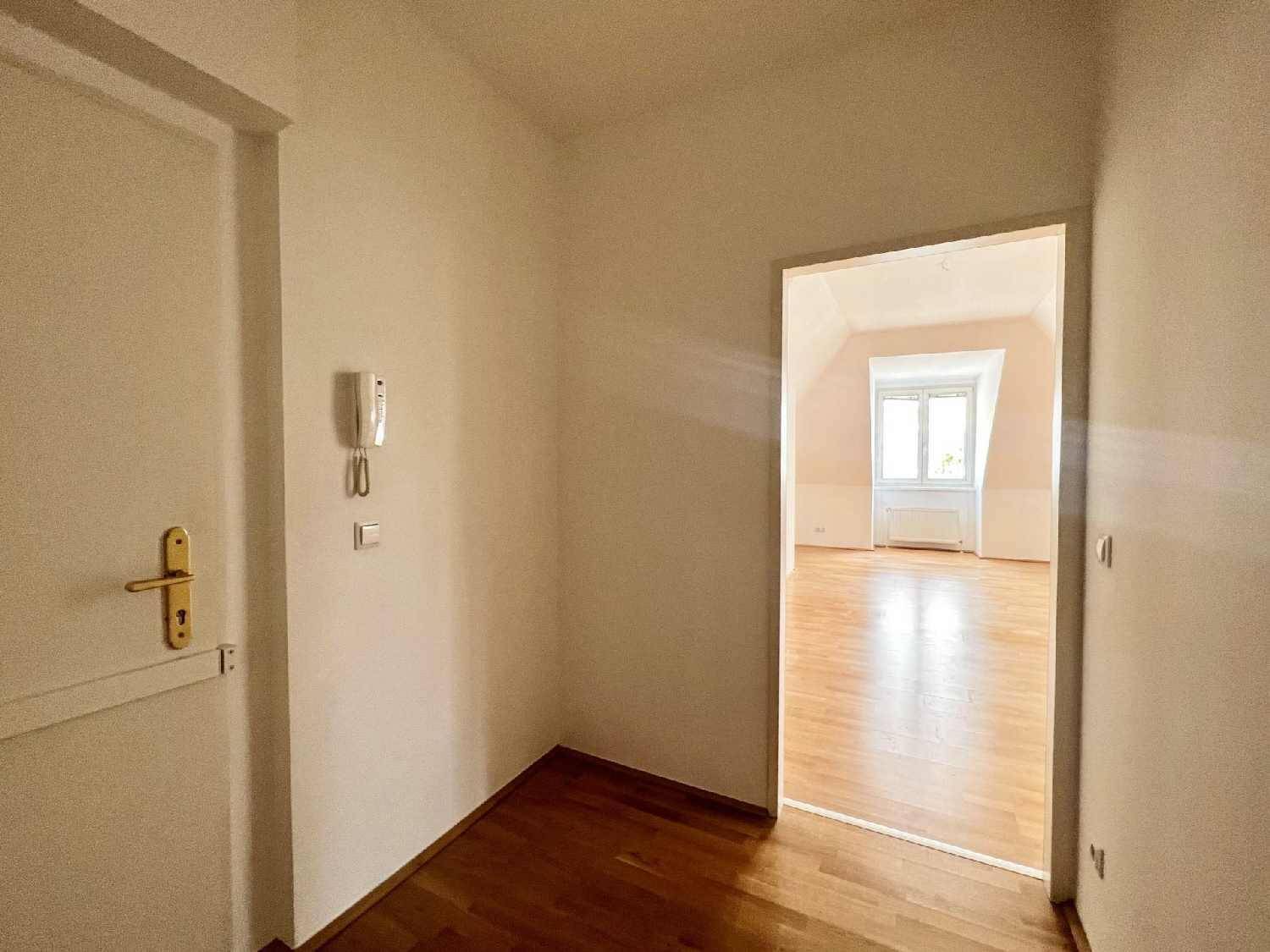 Eingangsbereich mit Intercom und Zugang zu einem hellen Zimmer mit Holzboden.