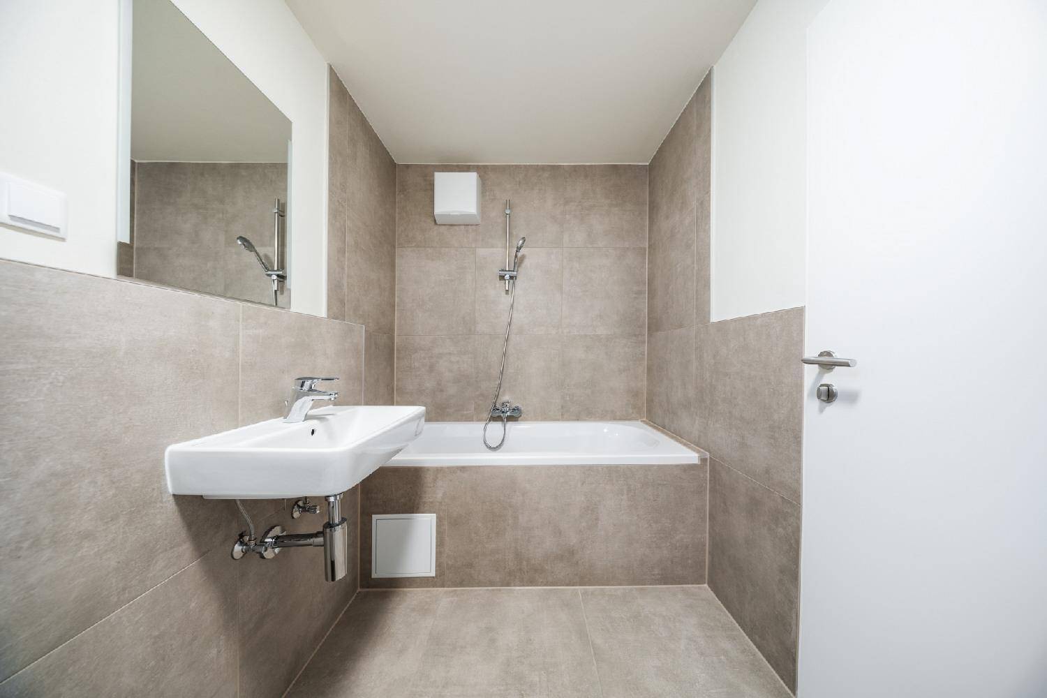 Modernes Badezimmer mit Badewanne, Waschbecken und großen grauen Fliesen an Wänden und Boden.