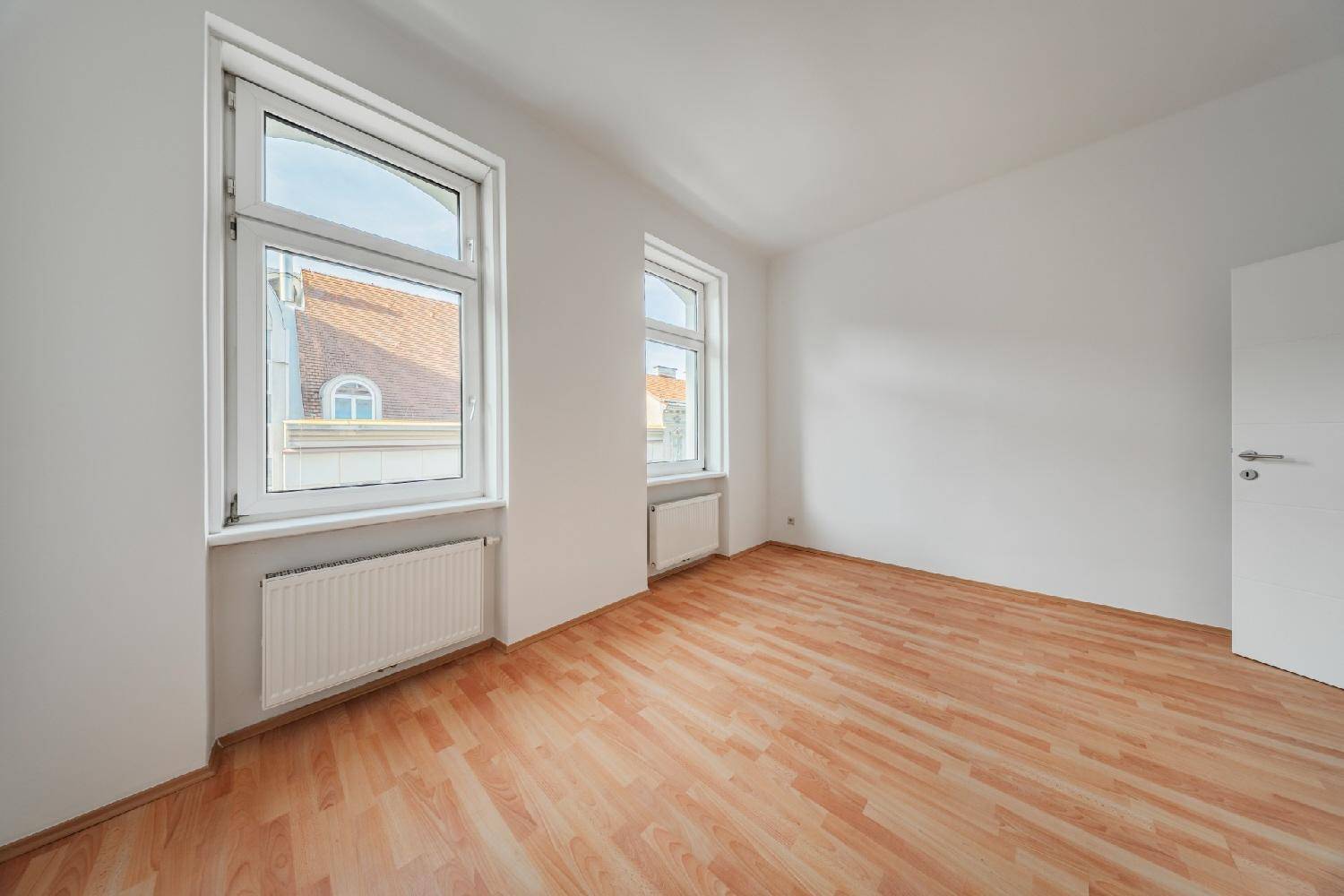 Geräumiges Zimmer mit Laminatboden und großen Fenstern, die viel Tageslicht hereinlassen.