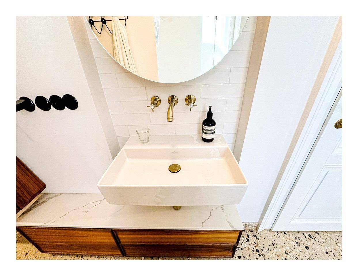Modernes Badezimmer mit stilvollem Waschbecken, goldenen Armaturen und Terrazzoboden.