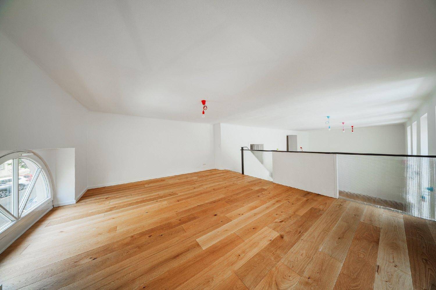 Geräumiger Wohnbereich mit Holzboden, hohen Decken und einem großen Rundbogenfenster, das viel Licht spendet.