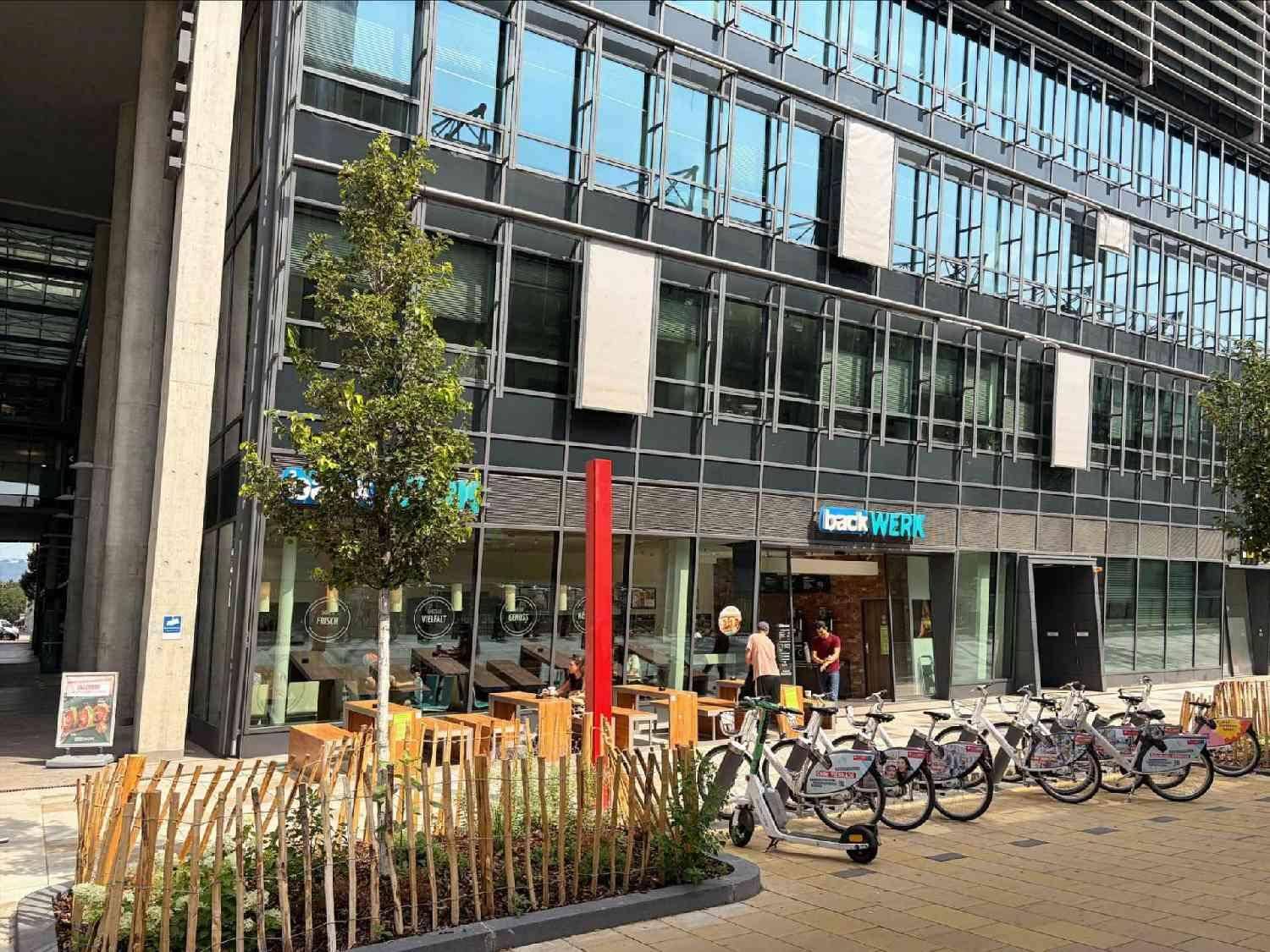 Ansicht der modernen Geschäftsfassade mit Bäumen, Fahrradständern und Außensitzgelegenheiten.