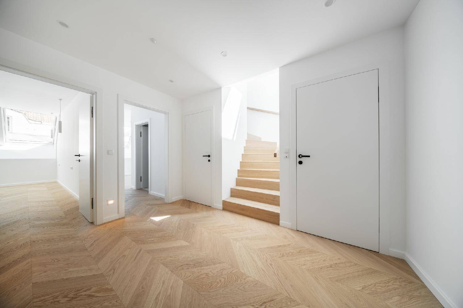 Heller Flur mit Fischgrätparkett und einer eleganten Holztreppe, die in die oberen Etagen führt.