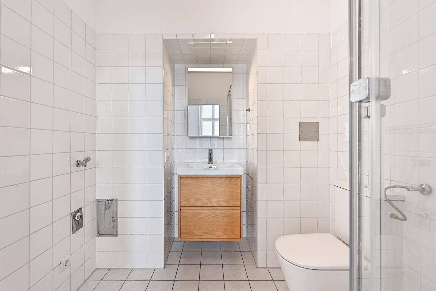 Modernes Badezimmer mit weißen Fliesen, schwebendem Waschtisch und einer Duschkabine.