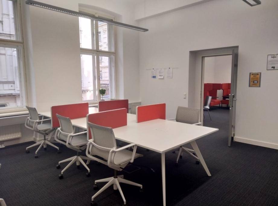 Modernes Büro mit mehreren Arbeitsplätzen, großen Fenstern und Teppichboden, ideal für Teamarbeit.