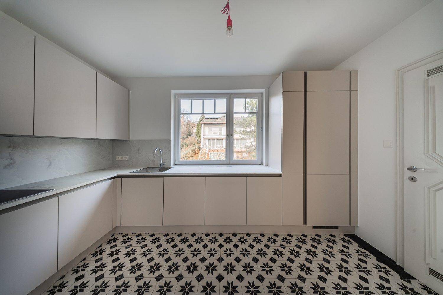 Moderne Einbauküche mit hellen Schränken, viel Arbeitsfläche und Blick ins Grüne durch das Fenster.