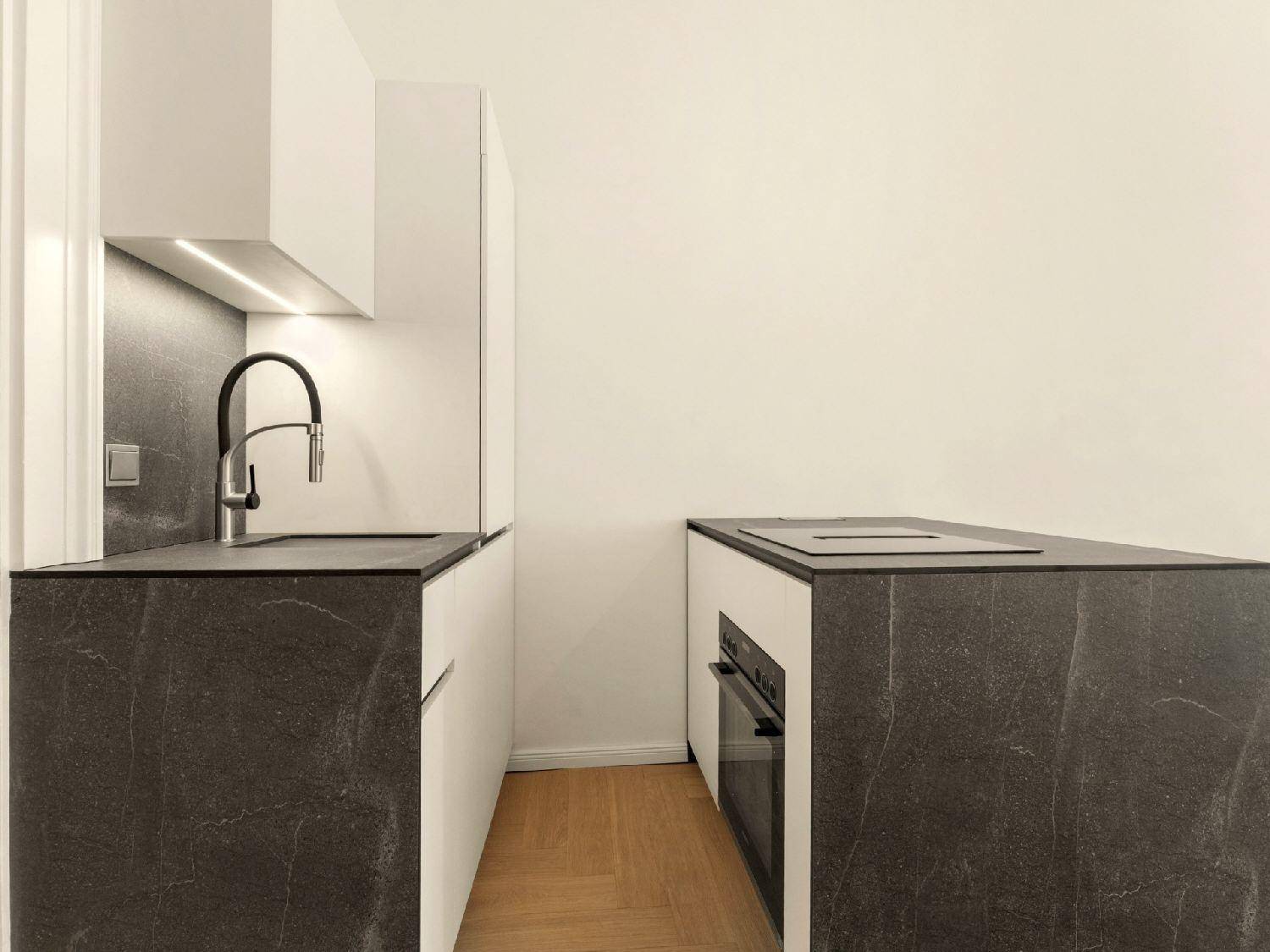 Kompakte Küchenzeile mit Spüle, Backofen und dunkler Arbeitsplatte in minimalistischem Design.