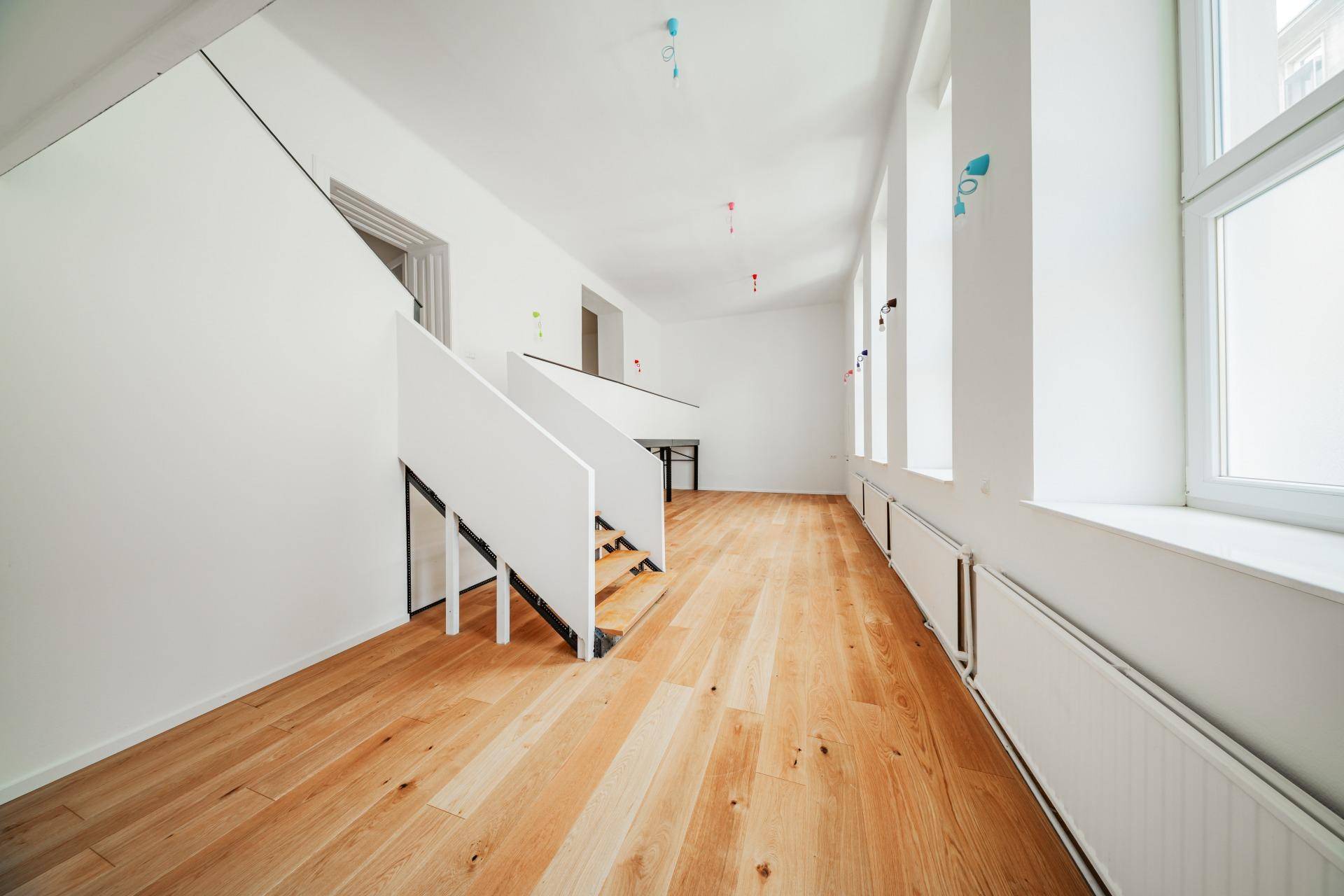 Langer, heller Raum mit Holzboden und Treppe, viele Fenster sorgen für eine freundliche Atmosphäre.