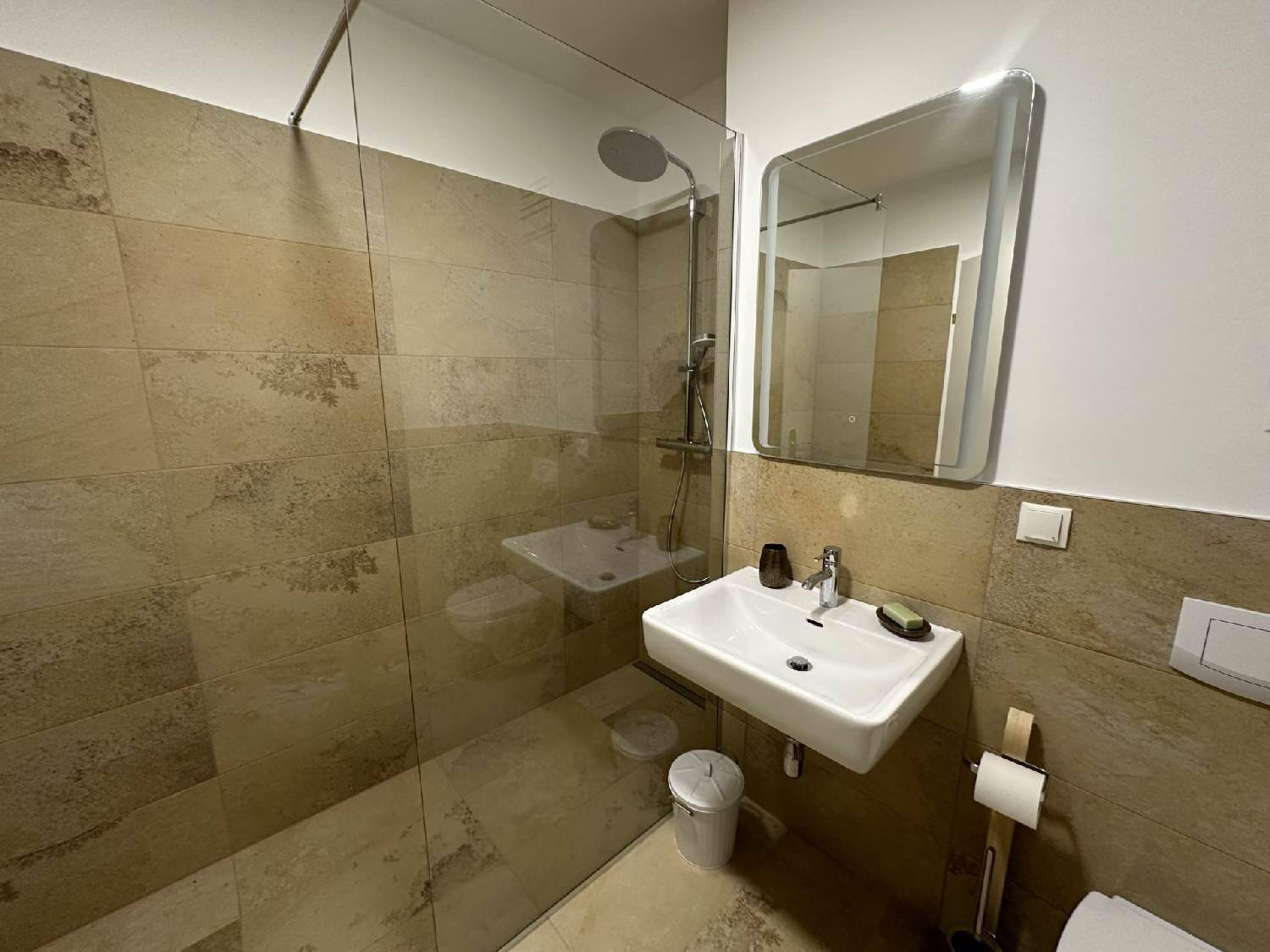 Modernes Badezimmer mit begehbarer Dusche, Wandwaschbecken und beigefarbenen Fliesen.