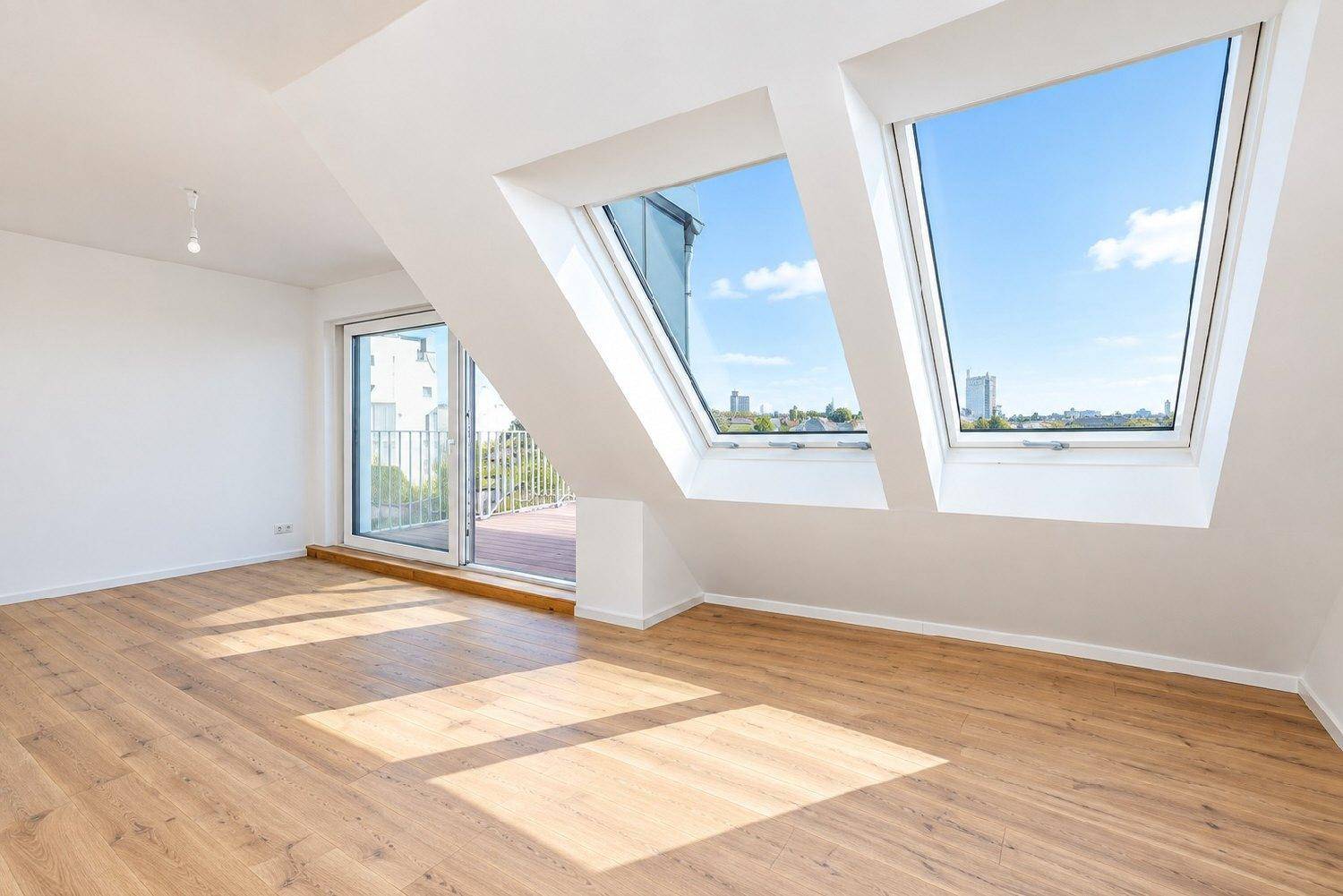 Heller Wohnraum im Dachgeschoss mit großen Dachfenstern, Laminatboden und Zugang zur Terrasse.