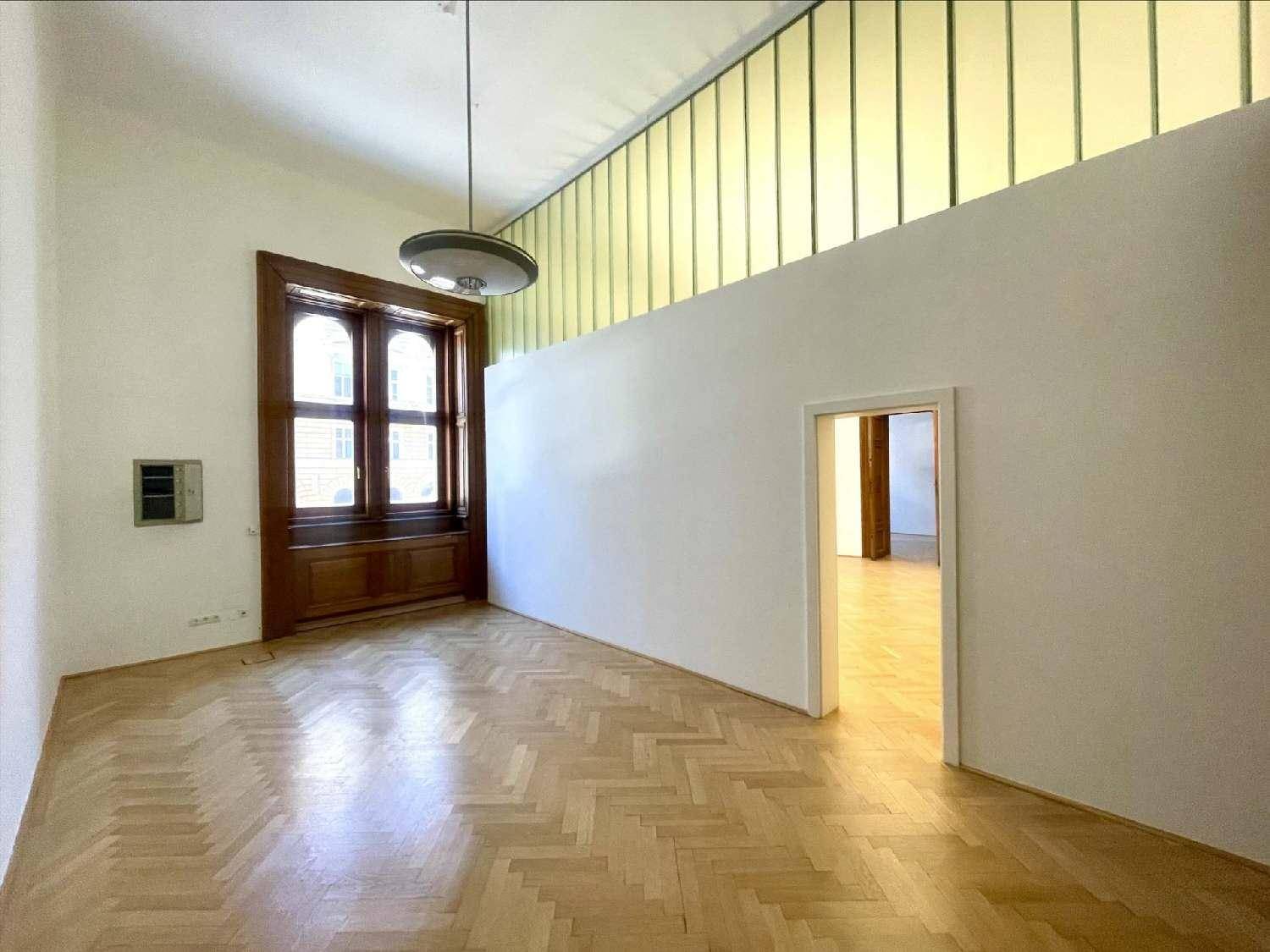 Heller Büroraum mit Fischgrätparkett, hohen Decken und einer Glaswand im oberen Bereich.