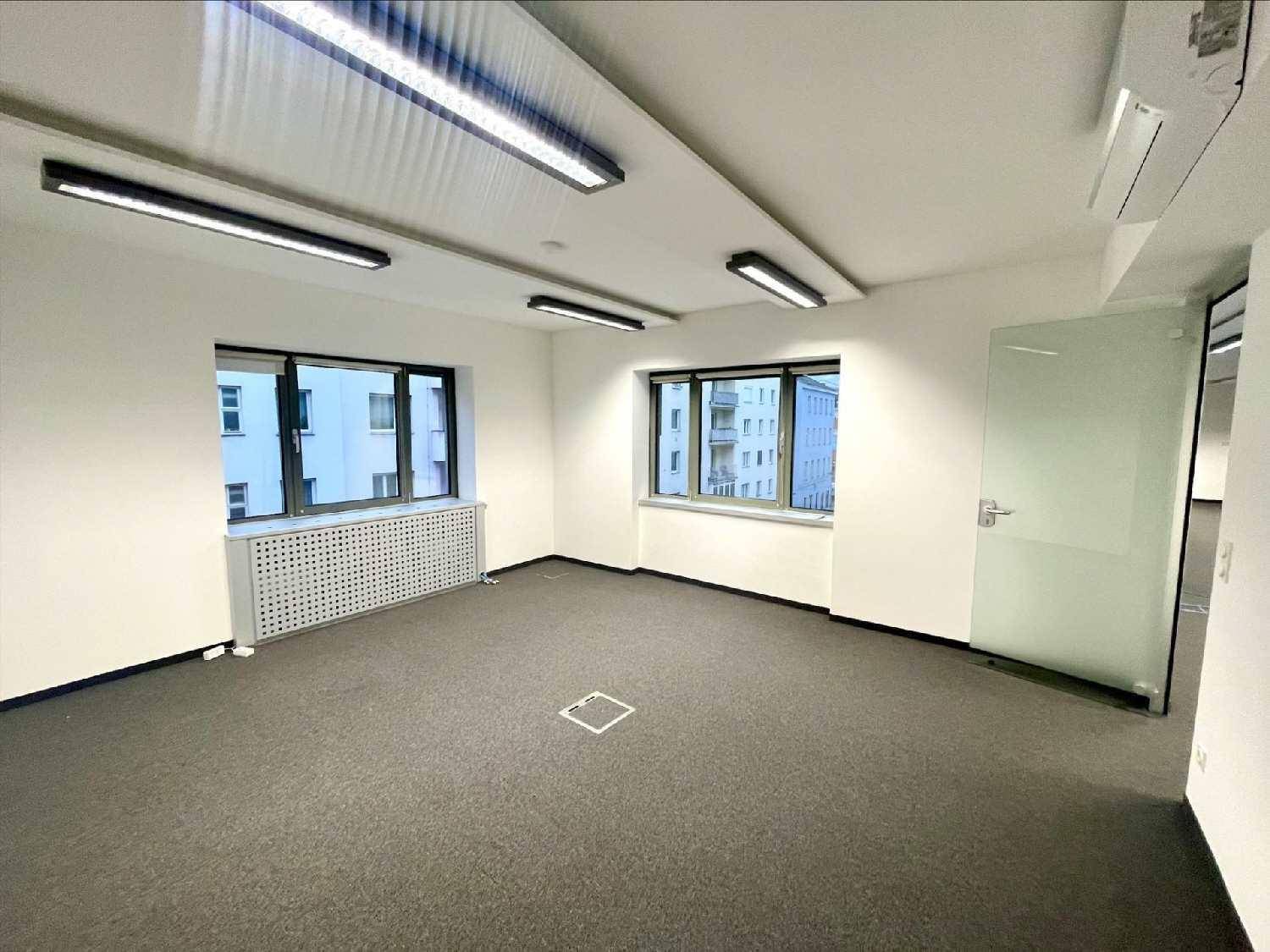 Heller Büroraum mit Teppichboden, Fenstern und einer Glastür zu einem weiteren Bereich.