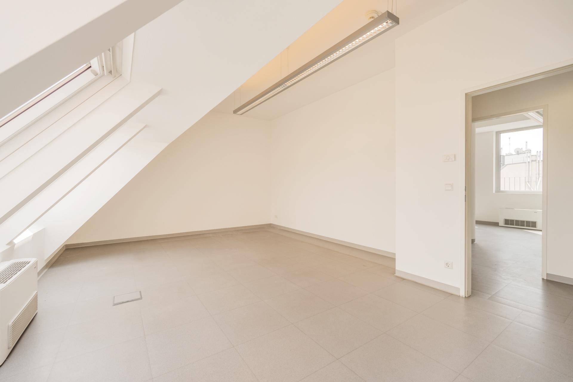 Dachgeschoss-Büroraum mit schräger Decke, Dachfenster und Zugang zu einem weiteren Bereich.
