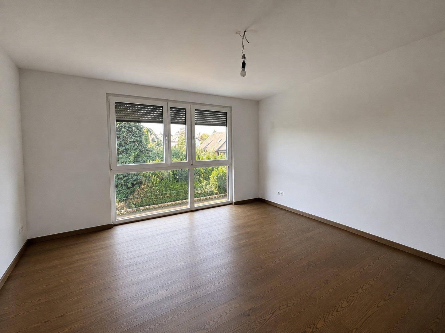 Geräumiges Zimmer mit Holzboden, großen Fenstern und Außenrollläden.