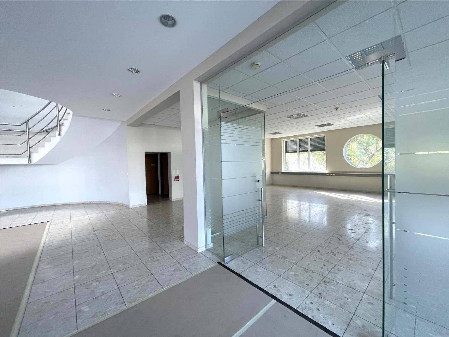 Heller Empfangsbereich mit Fliesenboden, Glasbüros und geschwungener Treppe im Hintergrund.