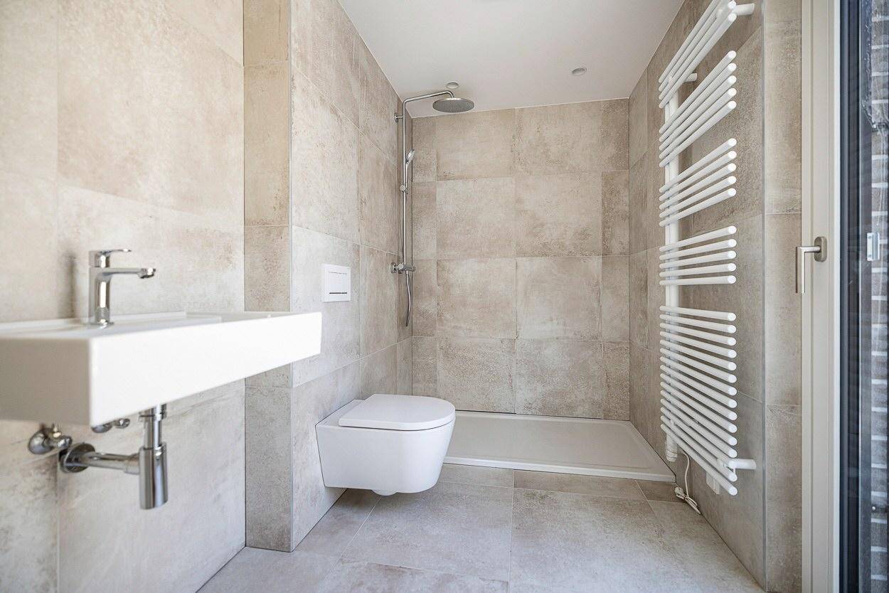 Zeitgemäßes Badezimmer mit wandhängendem WC, begehbarer Dusche und Handtuchheizkörper.