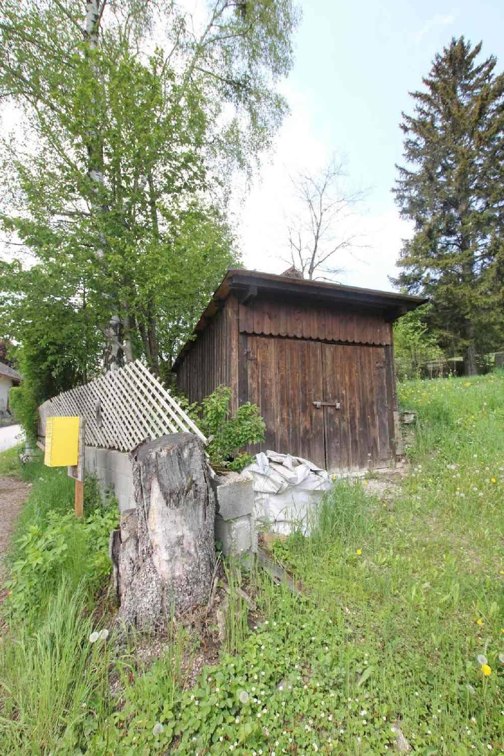 Rustikaler Holzschuppen im Gartenbereich, umgeben von Bäumen und Grünflächen.