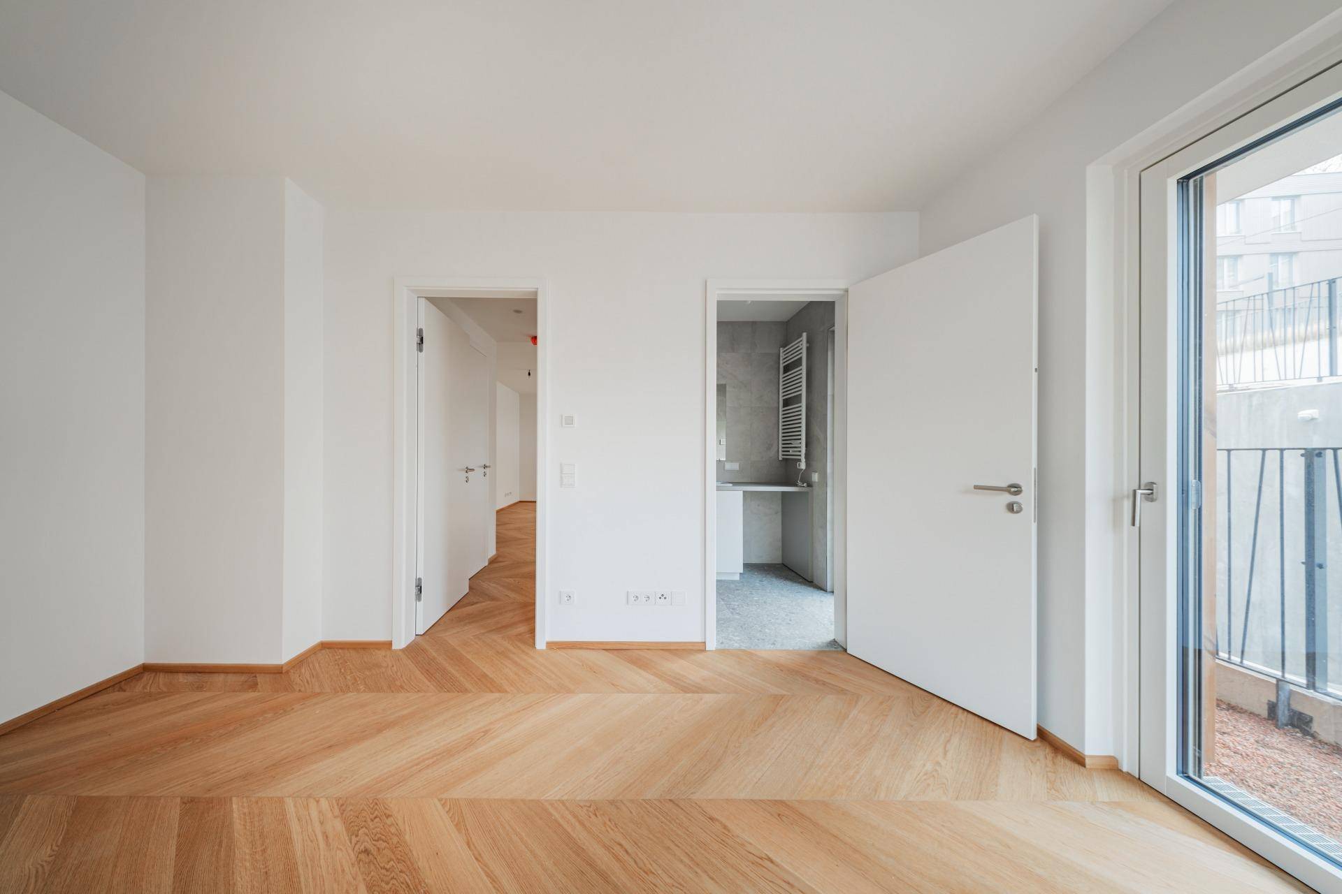 Geräumiges Zimmer mit Fischgrätparkett, weißen Wänden und Türen zu weiteren Räumen.