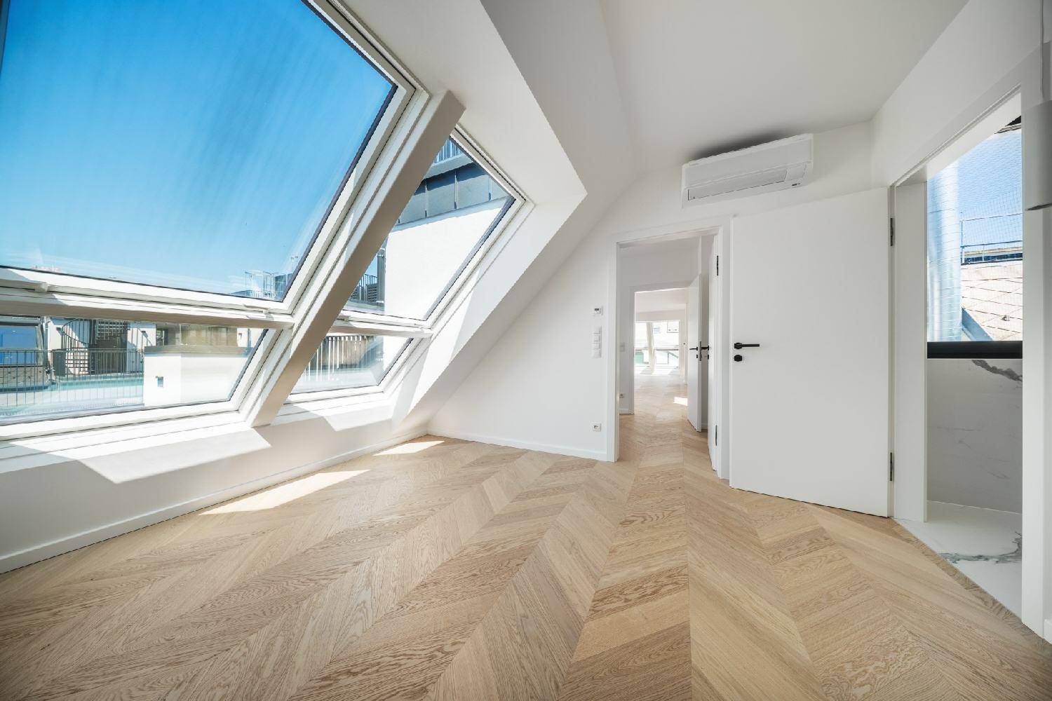 Helles Zimmer im Dachgeschoss mit schrägen Wänden, Dachfenstern und elegantem Fischgrätparkett.