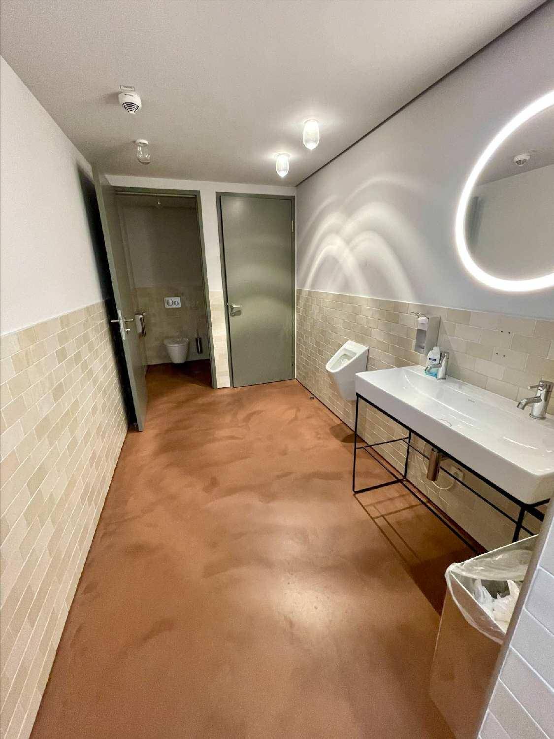 Modernes WC mit Urinal, Waschbecken und beleuchtetem Spiegel.