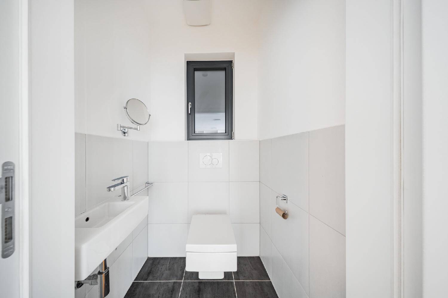 Kleines Gäste-WC mit wandhängender Toilette, Waschbecken und Fenster für natürliche Belüftung.