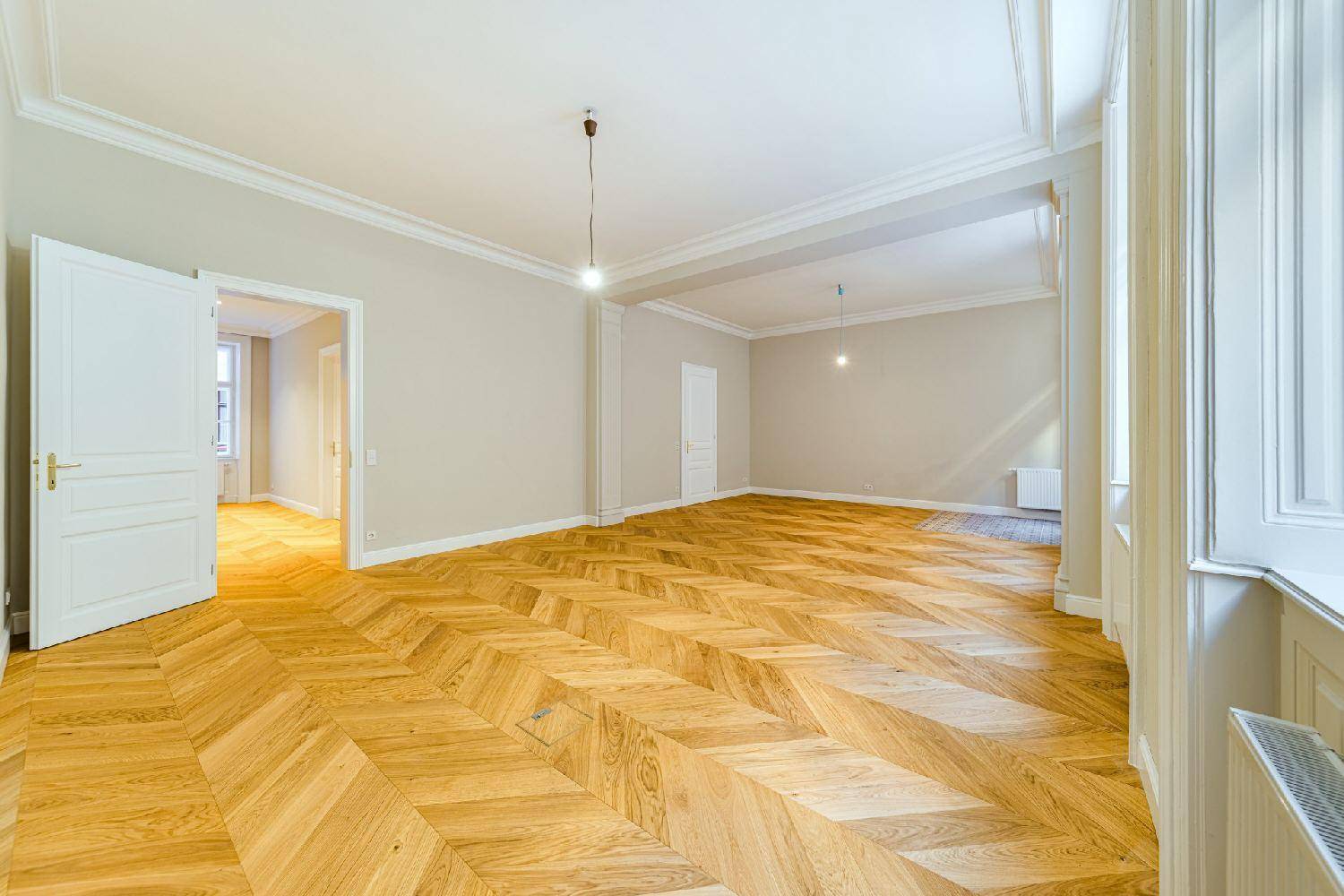 Großer, heller Wohnraum mit Fischgrätparkett, hohen Decken und klassischen Fenstern, die viel Licht spenden.