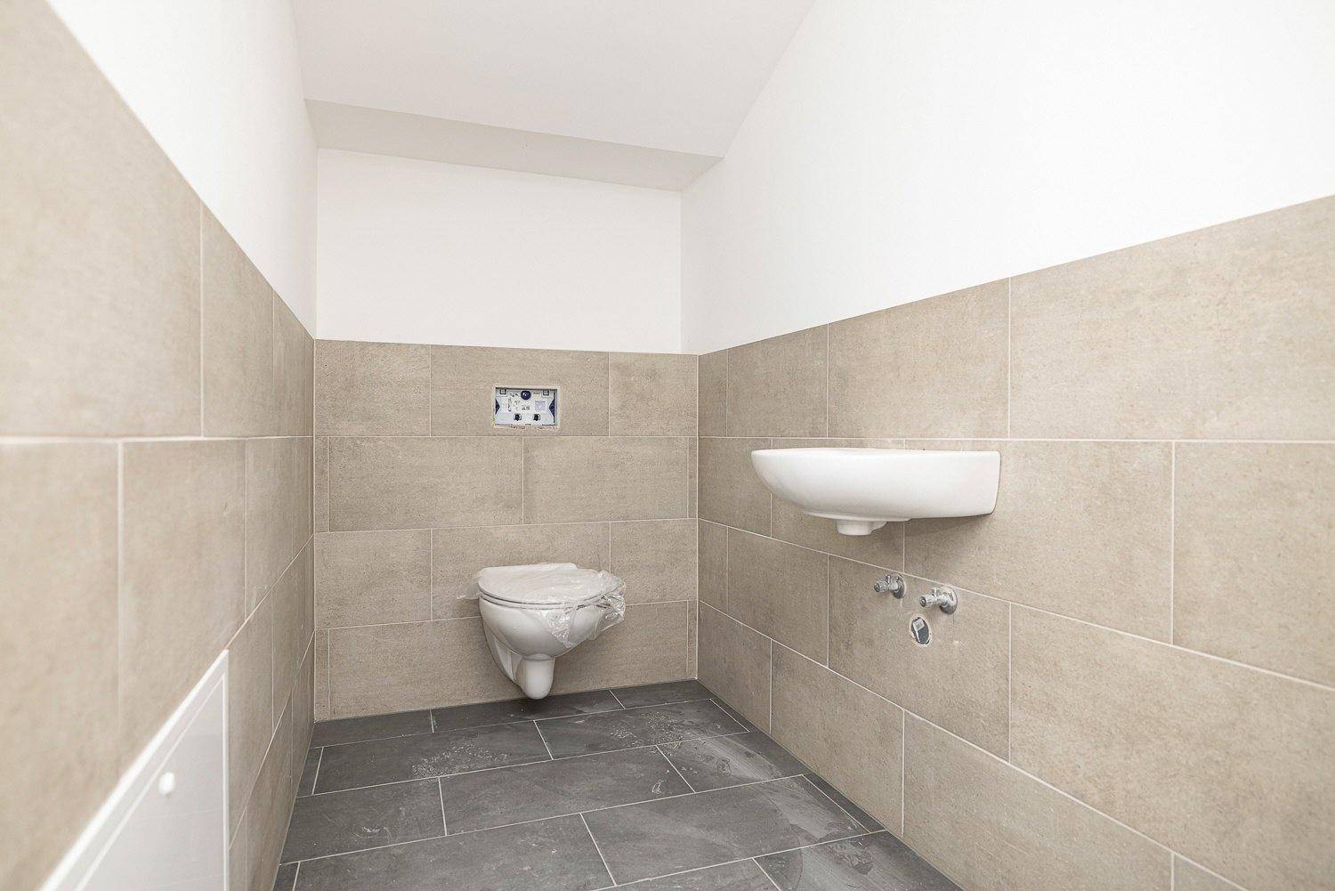 Gäste-WC im Bau mit Wand-WC, Waschbecken und modernen Fliesen an Wänden und Boden.