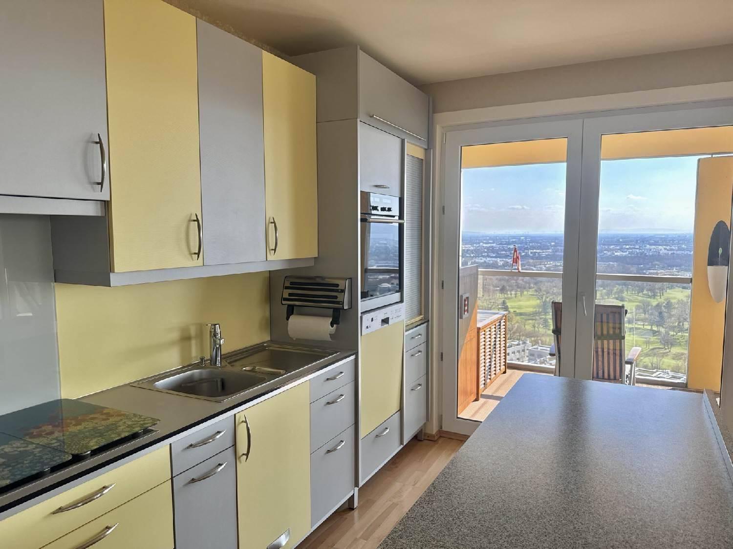 Funktionale Küche mit gelb-grauen Schränken, Einbaugeräten und Zugang zum Balkon.