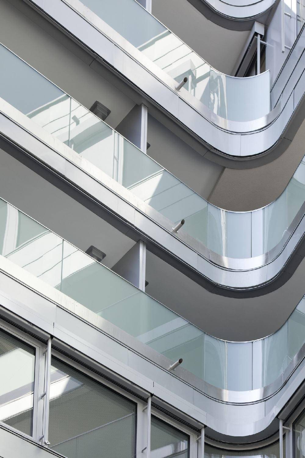 Nahaufnahme der geschwungenen Balkone mit Glasbrüstungen an der modernen Gebäudefassade.