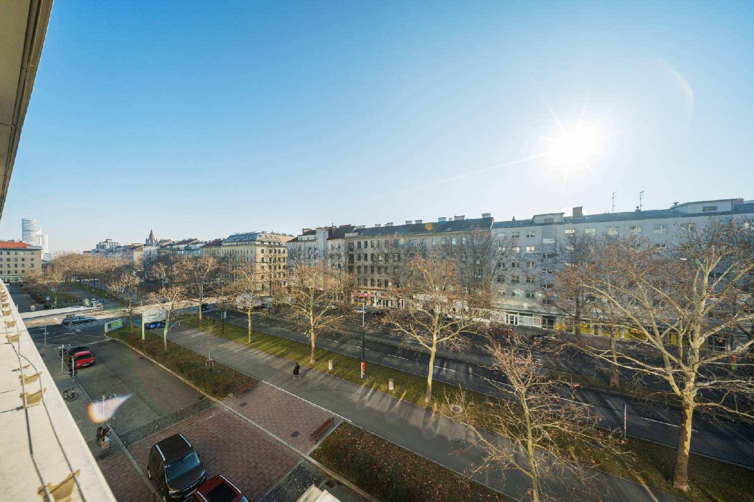 Weitläufiger Stadtblick von oben mit Gebäuden, Bäumen und sonnigem Himmel.