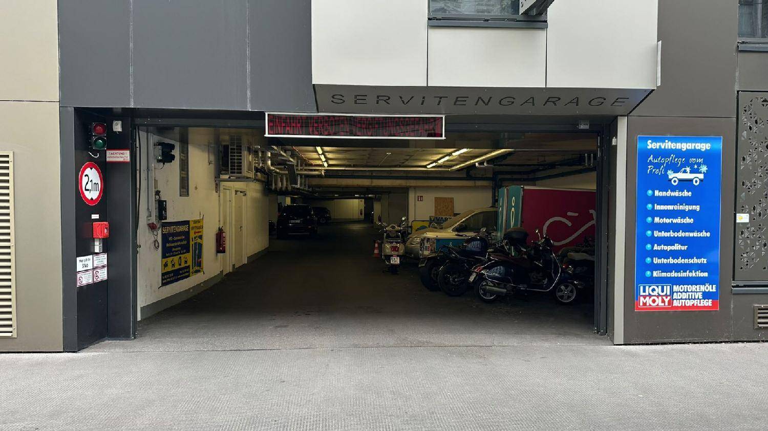 Eingangsbereich einer Servitengarage mit Rampe und Hinweisschildern in urbaner Umgebung.