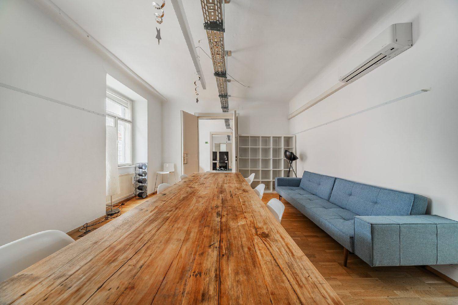 Großer Essbereich mit rustikalem Holztisch, blauer Couch und Regalen an der Wand.