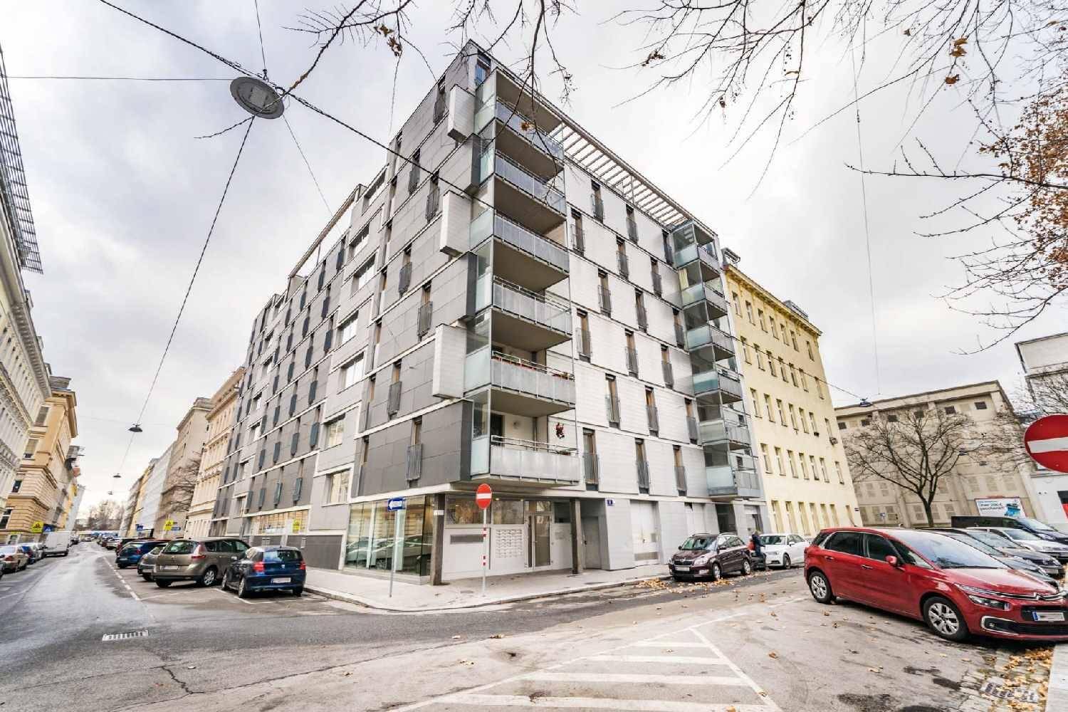 Modernes Wohngebäude an einer Straßenecke mit vielen Balkonen, großen Fenstern und städtischer Umgebung.