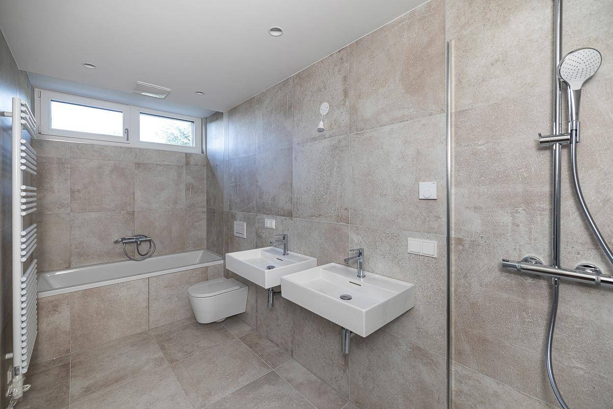 Modernes Badezimmer mit beigefarbenen Fliesen, Badewanne, Doppelwaschbecken und separater Dusche.