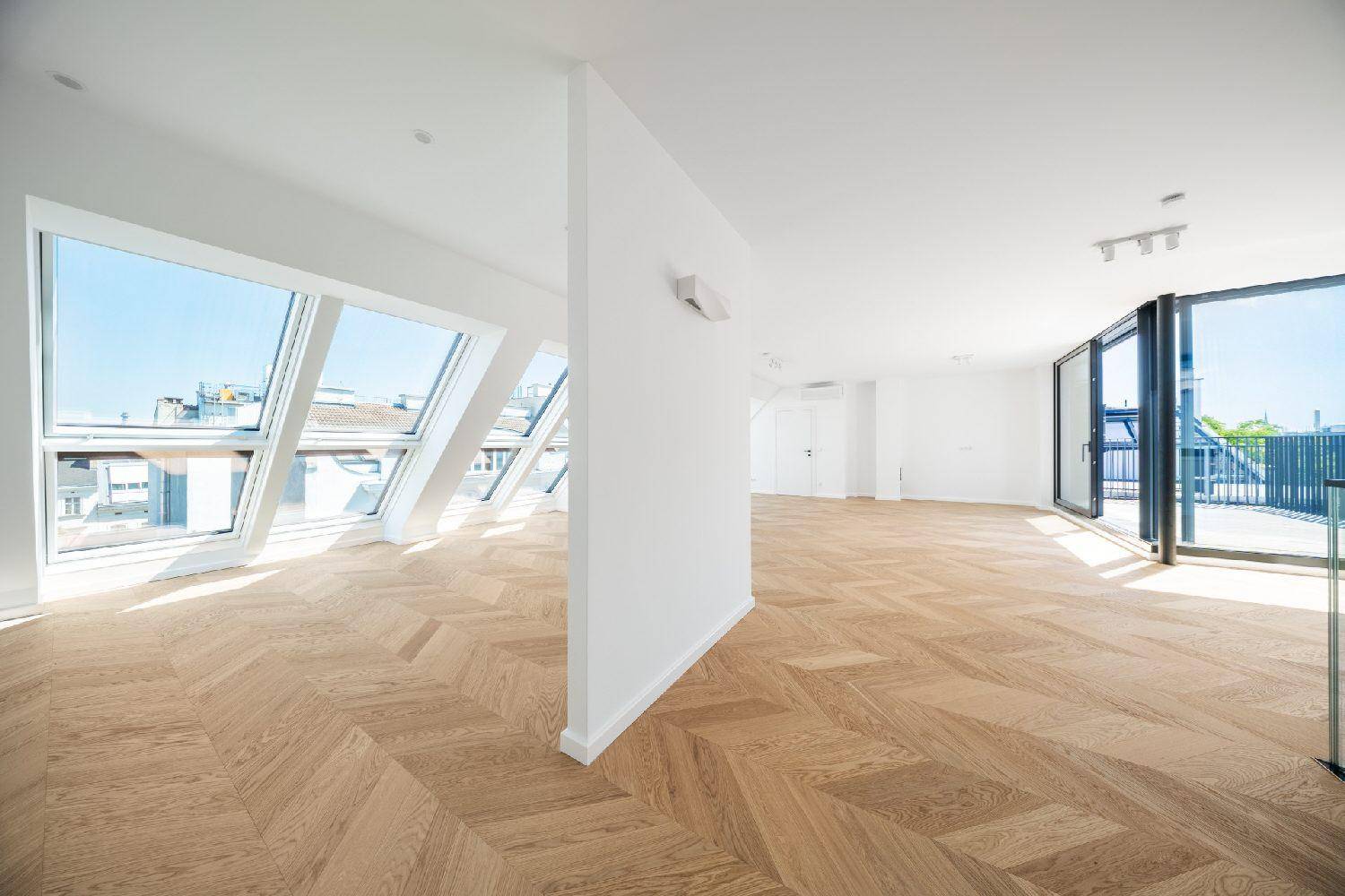Lichtdurchfluteter Wohnraum mit Fischgrätparkett und Zugang zu einer Terrasse durch große Glas-Schiebetüren.